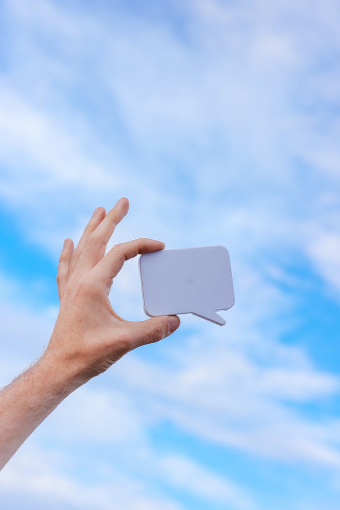 why-choose-us A hand holds a speech bubble icon against a clear blue sky, symbolizing communication.